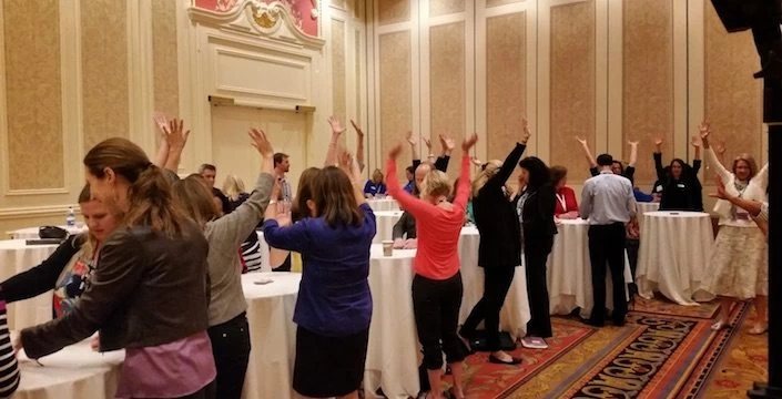A group of people raising their hands in a conference room.