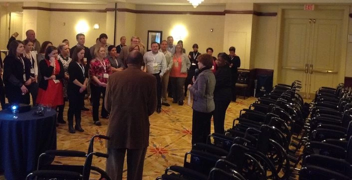 A group of people standing in a room with chairs.