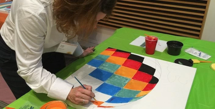 A woman painting a colorful ball on a table.