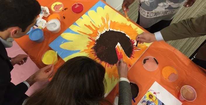 A group of people painting a sunflower on an orange table.