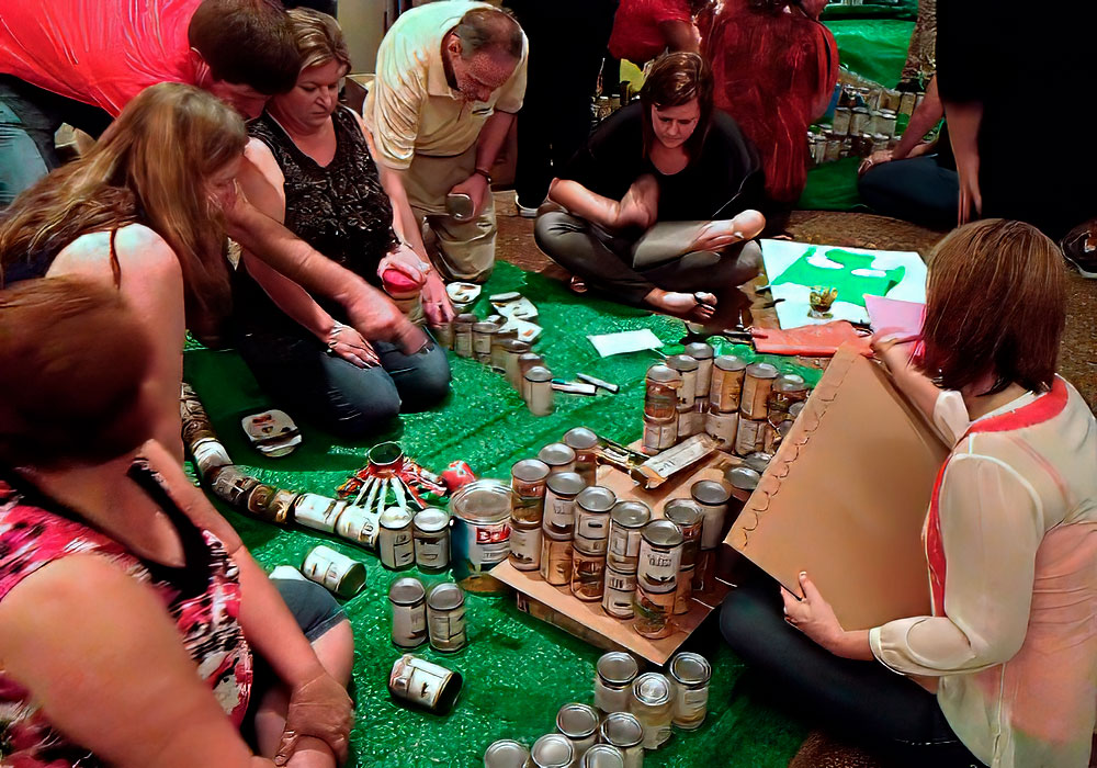 A group of people sitting around a table with cans of paint.