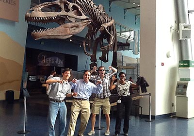 A group of people posing in front of a t - rex skeleton.