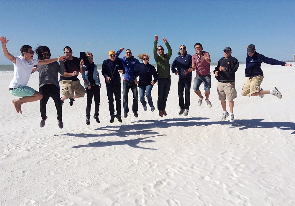 A group of people jumping in the air on a beach.
