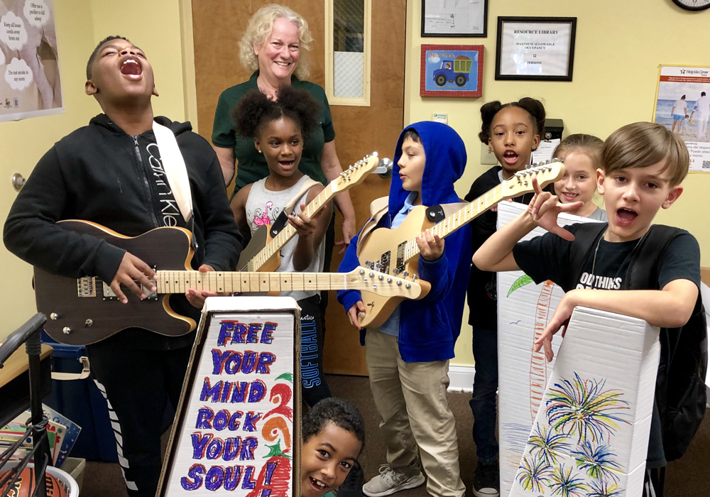 A group of children posing with guitars and signs.