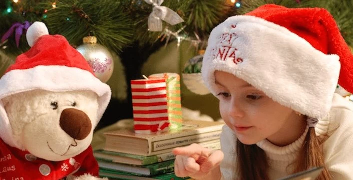 A girl with a santa hat and a teddy bear enjoying a book during a holiday party.