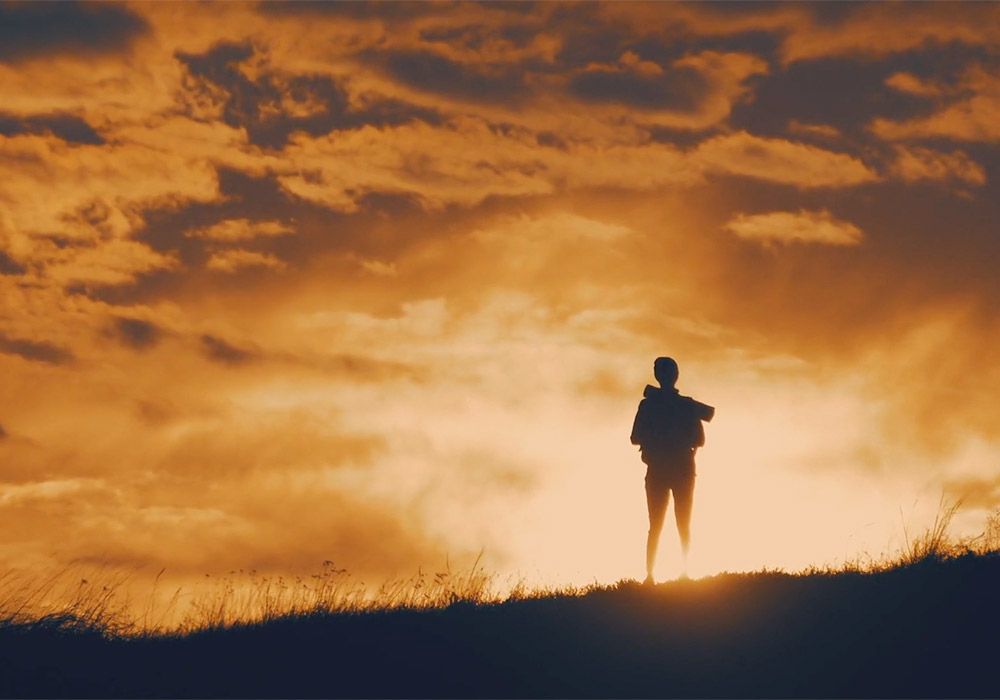 A silhouette of a person standing on a hill at sunset.