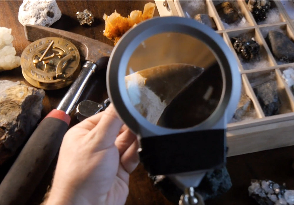 A person holding a magnifying glass over a table full of rocks.