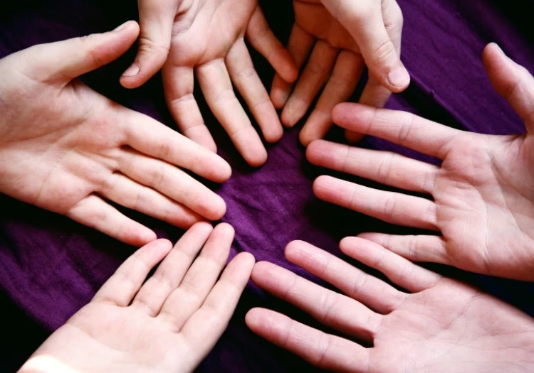 A group of hands forming a circle in a fun team activity on a purple background.