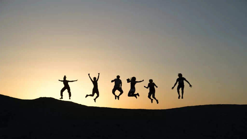 Silhouettes of people jumping in the air at sunset, promoting team building and boosting employee morale.