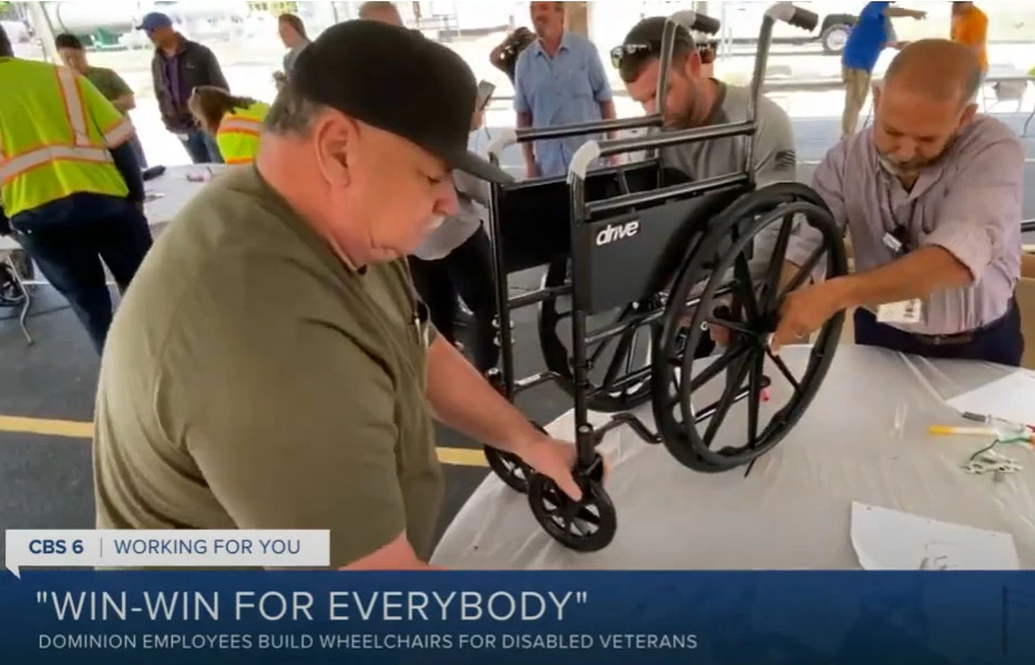 A man from Dominion Energy is working on a wheelchair in front of a group of people while showcasing their commitment towards building inclusive mobility solutions.