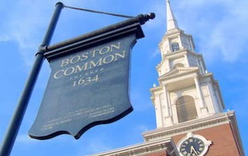A boston common sign with a clock tower in the background.